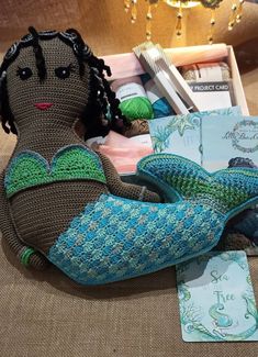 a crocheted mermaid doll sits on the floor next to books and knitting needles