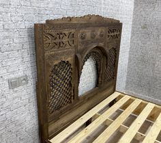 a wooden bed frame with intricate carvings on the top and bottom part, in front of a brick wall