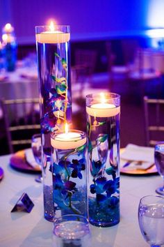 two tall glass vases filled with flowers and candles on top of a white table cloth