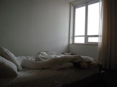 an unmade bed sitting in front of a window