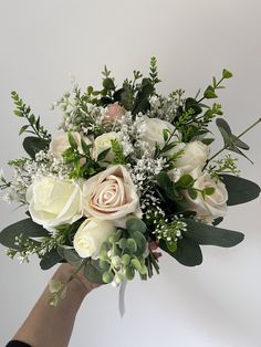 a hand holding a bouquet of white and pink flowers with greenery on the stems