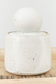 a white ceramic container sitting on top of a wooden table next to a black cat