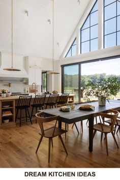 a large open kitchen and dining room area with wooden flooring, white walls and windows