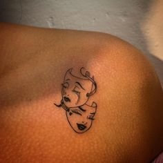 a woman's shoulder with a small tattoo of two faces on her left side