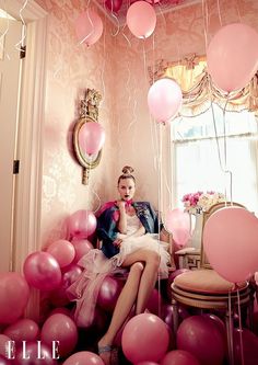 a woman sitting on a chair surrounded by balloons and streamers in a pink room