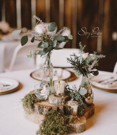 the table is set with white linens and greenery in vases on wood slices