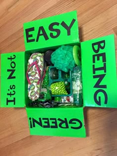 an open green box filled with assorted items on top of a wooden floor next to a sign that says easy being