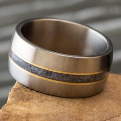 a close up of a ring on top of a piece of wood with a black and gold stripe