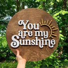 you are my sunshine wooden sign with hand - painted lettering in front of some trees