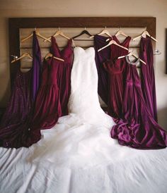 three dresses hanging on clothes pins in front of a bed with white sheets and purple drapes