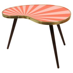 a pink and gold coffee table with an oval shaped design on the top, sitting in front of a white background