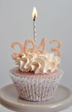 a cupcake with a lit candle on it sitting on a cake plate in front of a white wall