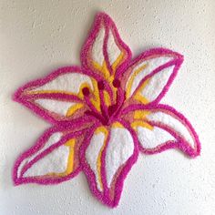 a pink and yellow flower is hanging on the wall in front of a white wall