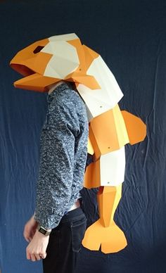 a man standing in front of a blue backdrop wearing a paper mask with an orange fish on it's head