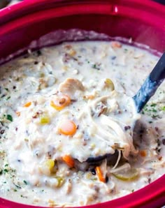 a red bowl filled with chicken and vegetable chowdery next to a blue spoon