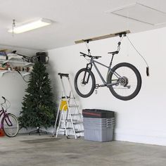 a bike hanging from the ceiling in a garage with christmas tree and ladders next to it