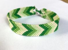 This hand-tied bracelet features an ombre chevron (V) pattern (in green or purple) and a toggle closure.  The green bracelet is 16 cm (~6.25 in) around and 1.5 cm (~5/8 in) wide. The purple bracelet is 16 cm (~6.25 in) around and 1.5 cm (~5/8 in) wide. Green Friendship Bracelets For Summer Gift, Green Summer Friendship Bracelets As Gift, Adjustable Green Friendship Bracelets, Adjustable Green Friendship Bracelets For Summer, Green Braided Bracelets As Summer Gifts, Handmade Green Bracelets For Summer, Handmade Green Friendship Bracelets For Summer, Green Friendship Bracelets For Summer, Trendy Green Friendship Bracelets As Gift