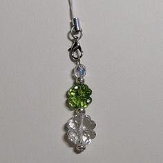 a green and white flower charm hanging from a silver plated hook on a chain