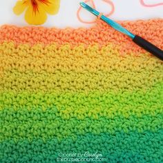 a crocheted rainbow blanket with a flower next to it and a paintbrush