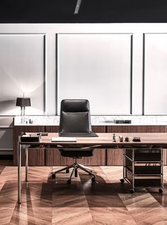 an office desk with a black leather chair in front of it on a hard wood floor