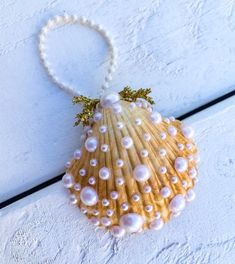 a seashell with pearls is hanging on a white wooden wall and has a beaded necklace attached to it