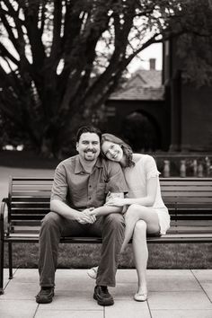 a man and woman sitting on a bench in front of a tree with their arms around each other