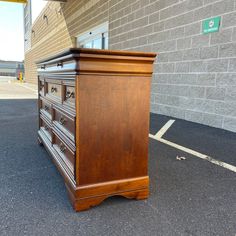 a wooden dresser sitting in front of a brick wall next to a parking lot with no one on it