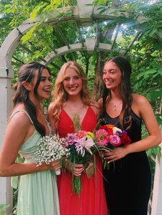 three beautiful young women standing next to each other in front of a gazebo holding flowers