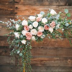 a bouquet of roses and greenery in front of a wooden wall with wood planks