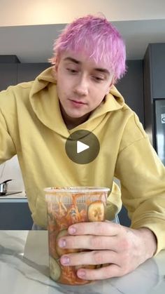 a man with pink hair sitting at a table in front of a cup filled with donuts