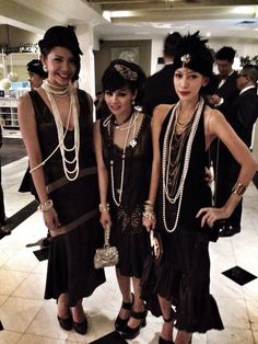 three women standing next to each other in black dresses and pearls on their necklaces