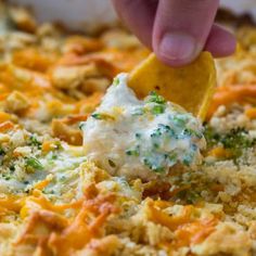 a person dipping a tortilla chip into a casserole dish with cheese and broccoli