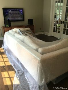 a couch covered in plastic sitting on top of a hard wood floor next to a tv