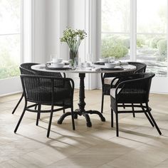 a table with four chairs around it in front of two large windows and a potted plant