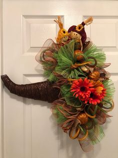 a wreath with two stuffed animals hanging on the front door, decorated with grass and orange flowers