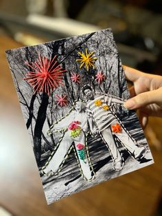 a person holding up a card with fireworks in the sky and two people on it