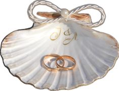 two gold wedding rings in a shell with the word joy written on it and an engraved ring holder