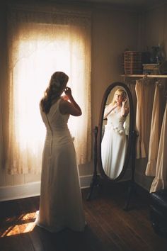 a woman standing in front of a mirror looking at her reflection wearing a wedding dress