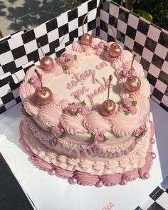 a pink birthday cake sitting on top of a checkerboard tablecloth covered box