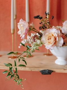 a white vase filled with flowers on top of a wooden table next to two candles