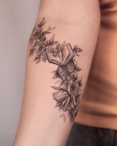 a woman's arm with an open book and flowers tattoo on her left arm