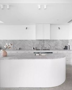 a white kitchen with marble counter tops and an island in front of the stove top