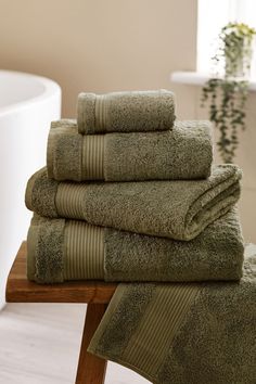 a stack of towels sitting on top of a wooden table next to a bath tub