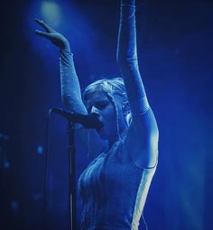 a woman holding her arms up in the air on stage with one hand raised above her head