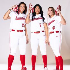 three women in red and white baseball uniforms posing for the camera with their hands on their hips