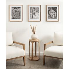 three framed pictures hang on the wall above two chairs and a table with a vase