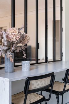 flowers in a vase sitting on a table next to two black chairs and a mirror