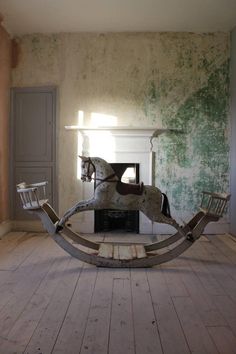 an old rocking horse in the middle of a room with peeling paint on the walls