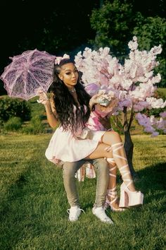 a woman sitting on top of a bench holding an umbrella next to a pink tree