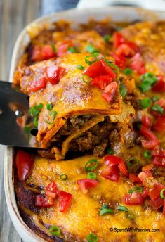 a casserole dish filled with meat, cheese and tomato slices being lifted from the casserole